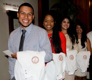 Four pharmacy students with white coats draped over their arms at white coat ceremony