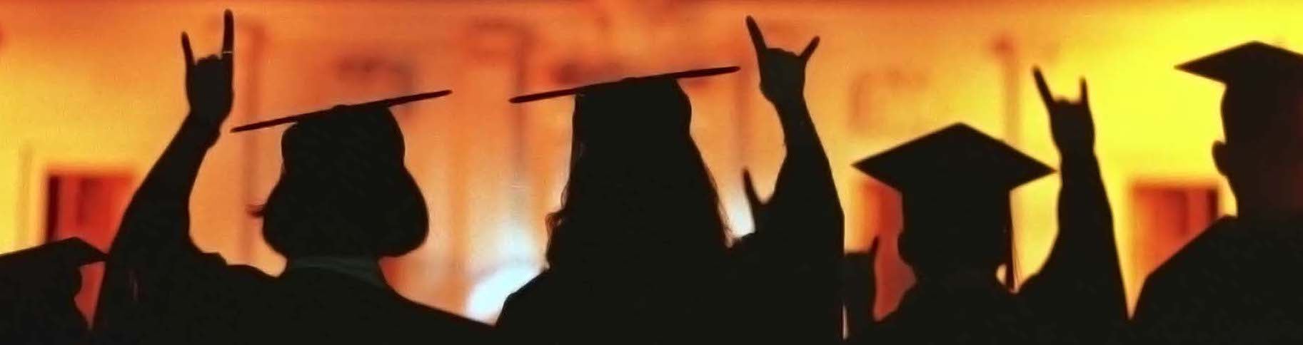 Night photo of graduates with hook-em hand sign