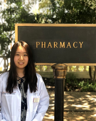 A woman smiling in front of a sign that says "Pharmacy."