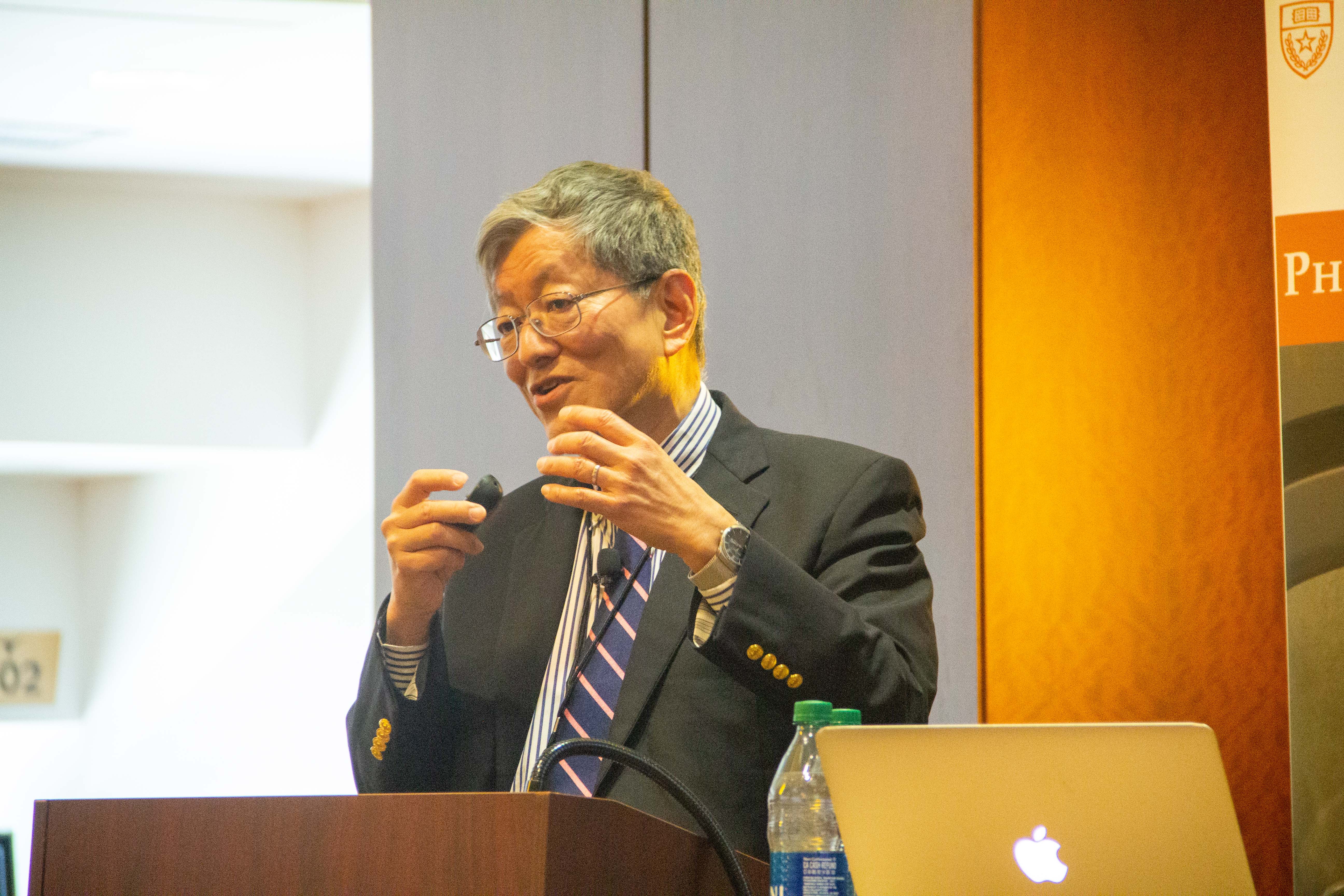 Professor Liu standing behind a podium with his laptop presenting.