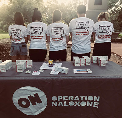 Operation Naloxone information table with students wearing t-shirts that say, "Stand up. Save a life."