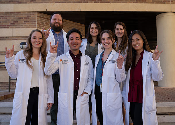 Pharmacotherapy graduate students group photo; students are wearing lab coats and standing on steps of building