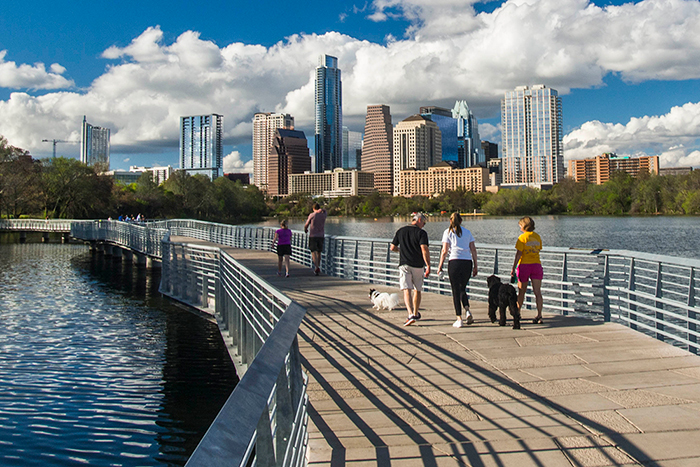 Austin skyline with bridge over river and people walking dogs along bridge