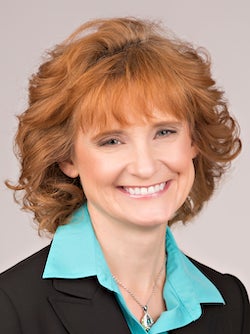 A woman smiling while wearing a blazer, collared shirt and necklace.