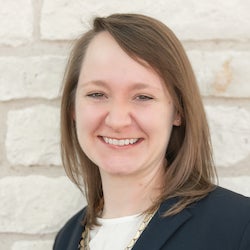 A woman smiling in front of a limestone wall.