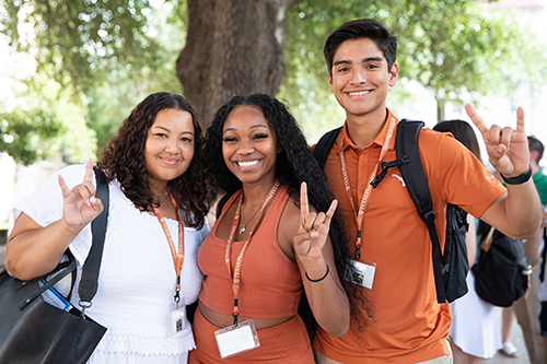 Three students at orientation smiling and giving Hook 'Em Horns hand sign