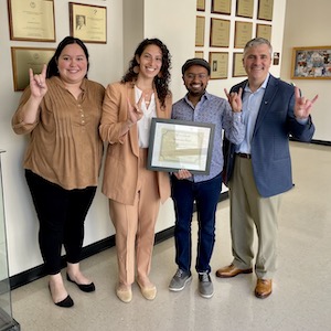 Four people giving the Hook 'em Horns hand gesture and holding a framed certificate.