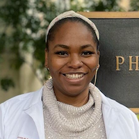 Amaka Epoh smiling in front of a sign that says pharmacy.