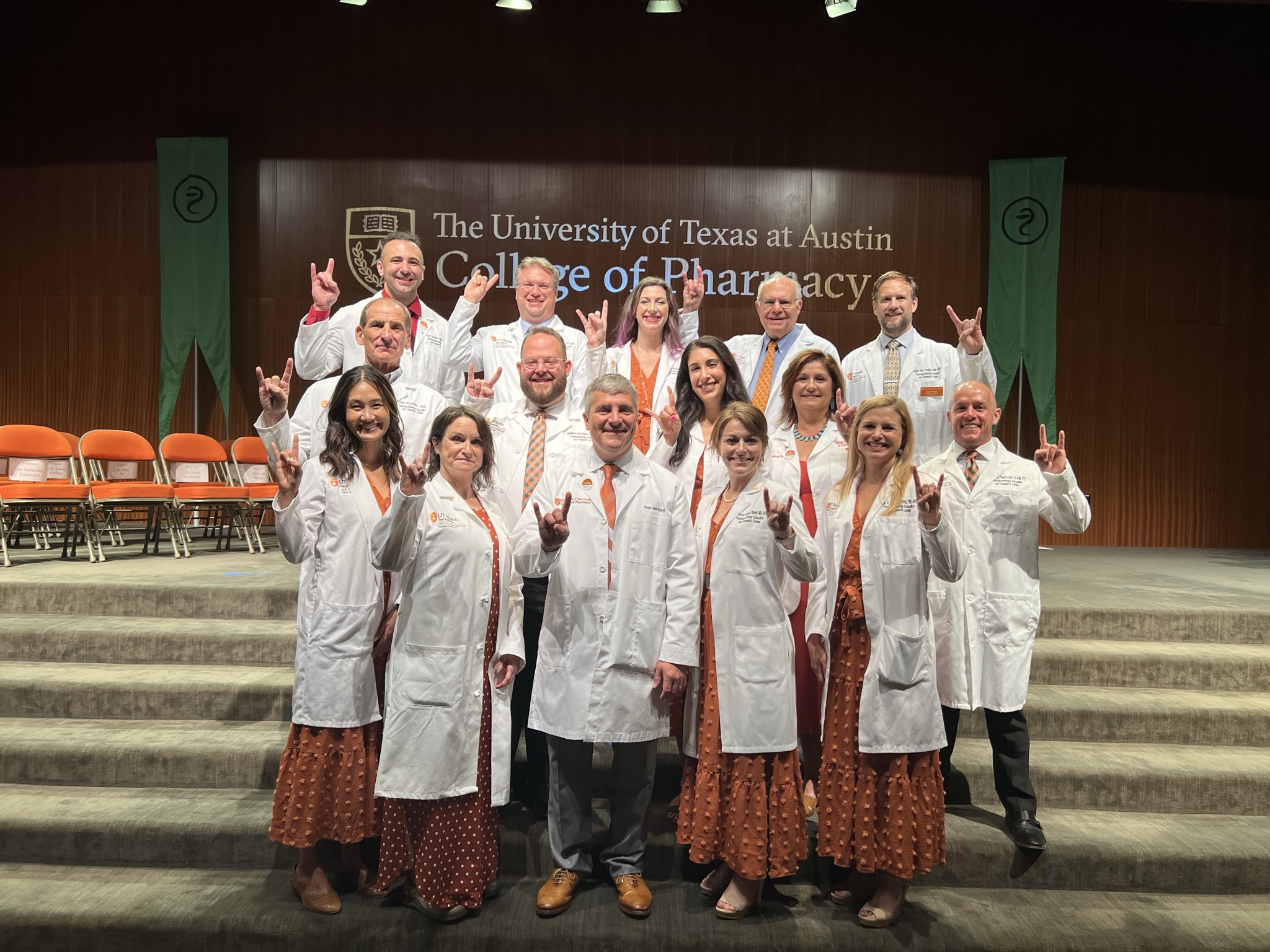 A group of people on some carpeted steps, wearing white coats and giving the Hook 'em Horns hand gesture.