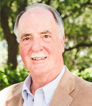 A man wearing a sport coat and collared shirt and smiling.