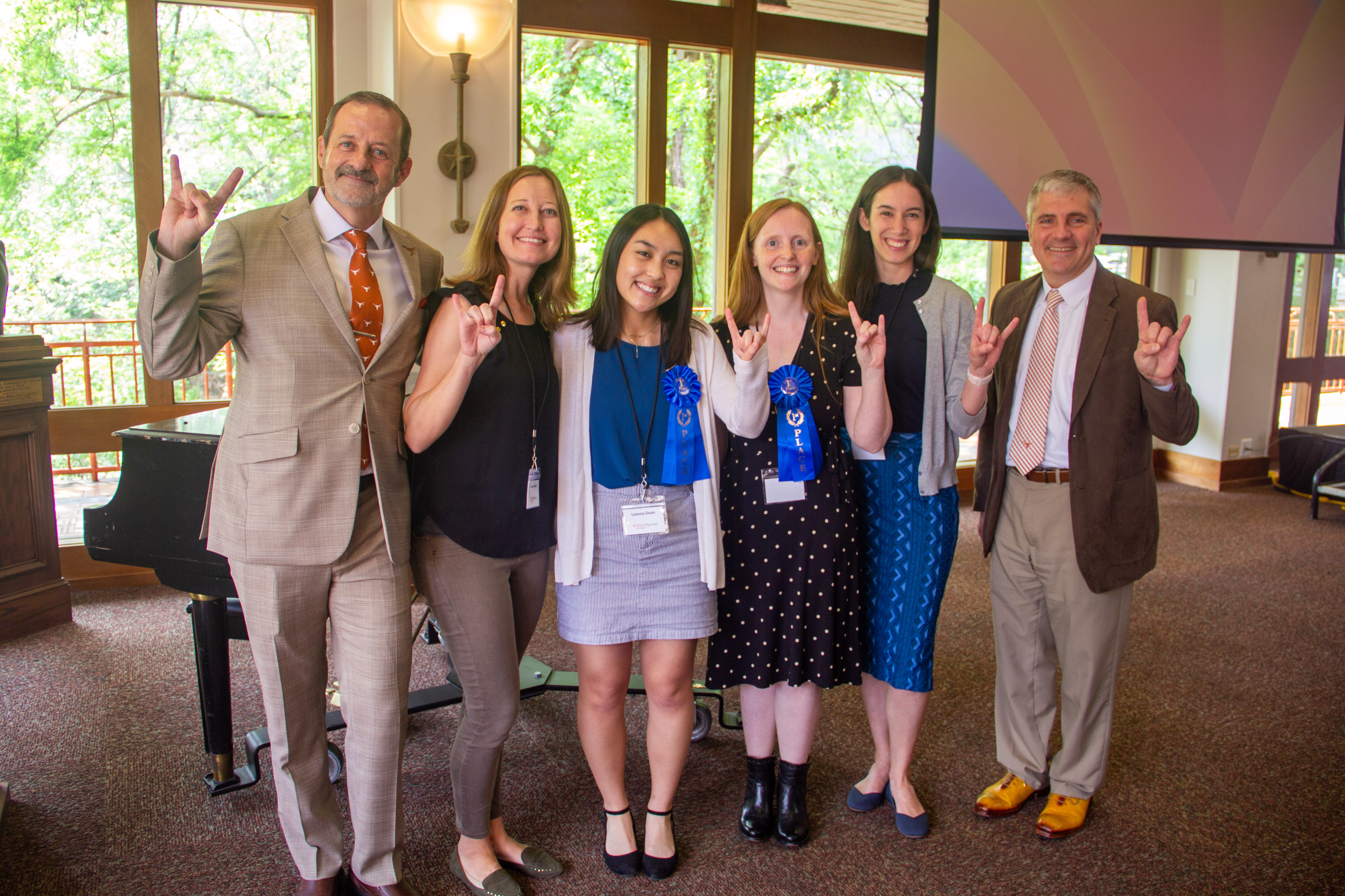 A group of people with blue ribbons giving the Hook 'em Horns hand gesture.