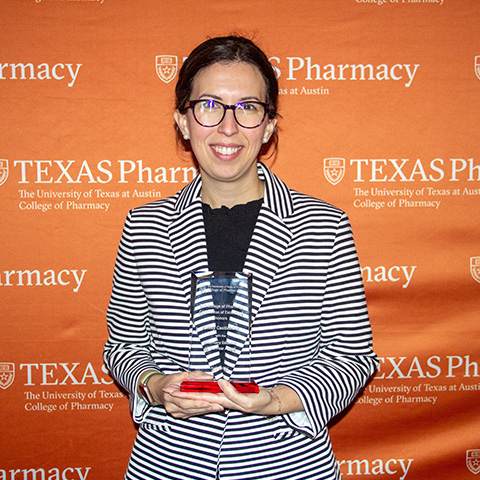 A woman wearing glasses and wearing a striped jacket while holding an award.