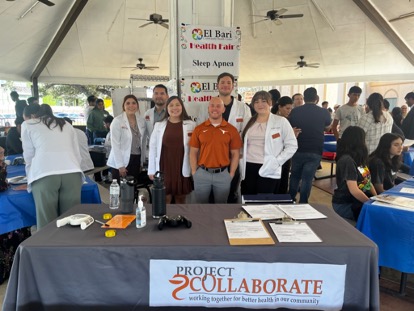 A group of people under a large party tent and standing at a table with a Project Collaborate sign.