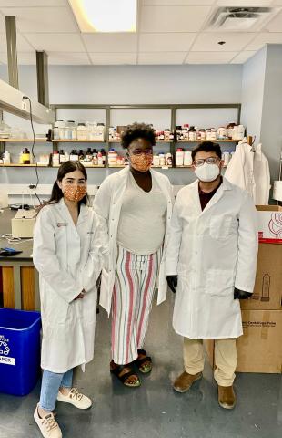 Three students in white coats in the lab.