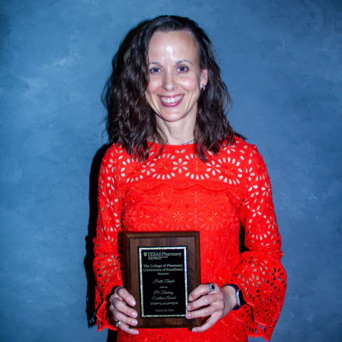 A photo of Dr. Holli Temple holding her award plaque. Dr. Temple has shoulder-length brown hair and is wearing a bright red dress with bell sleeves.