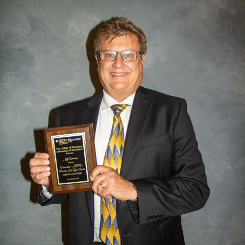 A photo of Jeff Warnken holding his award plaque. He is wearing a black suit jacket with a patterned yellow and grey tie.