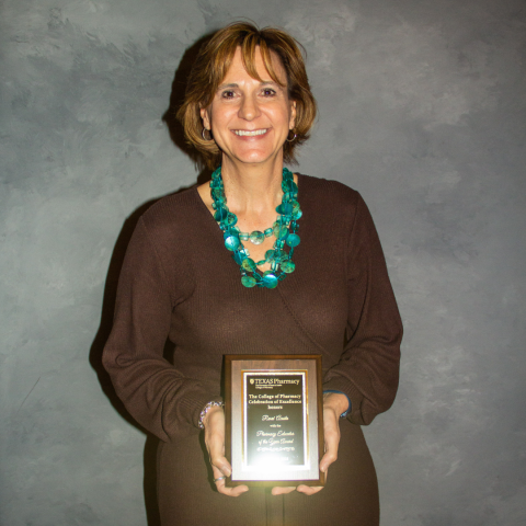 A photo of Renee' holding her award plaque. She is wearing a chocolate brown, long-sleeved dress with a turquoise statement necklace.