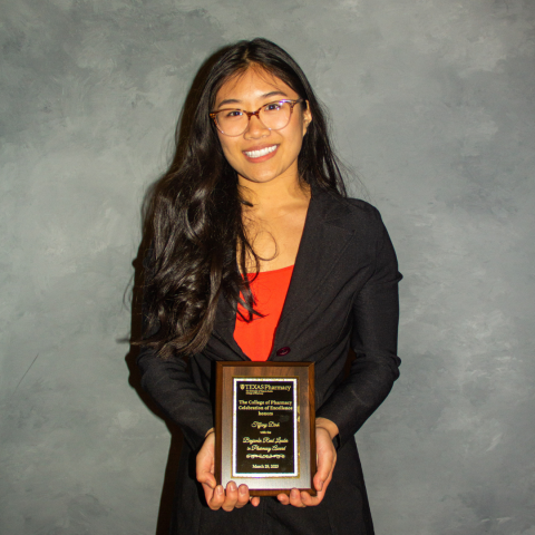 Tiffany Dinh holding her award plaque. She is wearing a black blazer over a red top. Tiffany has very long brown hair and is wearing wire-framed glasses.