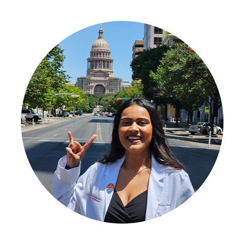 A woman standing on Congress Avenue giving the Hook 'em Horns hand gesture with the Texas Capitol in the background.
