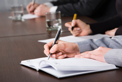 A side view of a hand holding a pen and writing on a sheet of paper. 