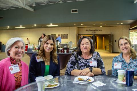 A group of four women sit at a table during the Preceptor Conference. They are all smiling and looking at the camera.