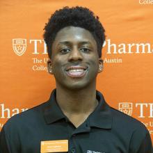 Seun Lagbenro smiling in front of an orange UT Pharmacy background