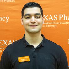 Thomas Peña smiling in front of an orange Texas Pharmacy background