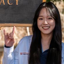 Sarah Zhou smiling and giving the Hook 'em Horns hand sign
