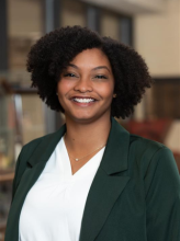 Headshot of Dr. Kiles. She has short, curly dark hair and is smiling to camera in a white shirt under a green blazer.