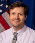 Dr. Brendon Hogan smiling in front of US flag