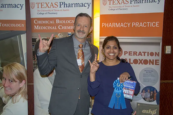 Dr. Richburg smiling and giving hook em horns sign with student winner at Research Day competition
