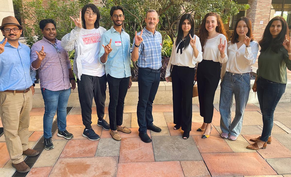 Dr. Richburg and lab members in outdoor photo smiling and giving hook em horns hand sign