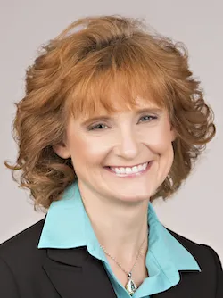 A woman smiling while wearing a blazer, collared shirt and necklace.