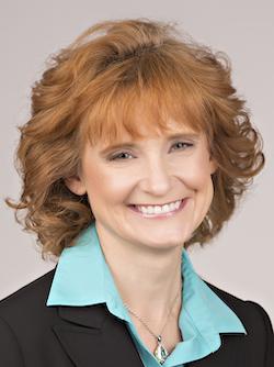 A woman smiling while wearing a blazer, collared shirt and necklace.