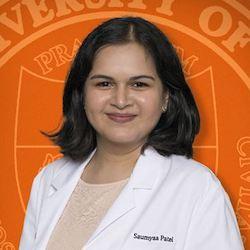 A woman smiling and wearing a white coat in front of the UT Austin seal.