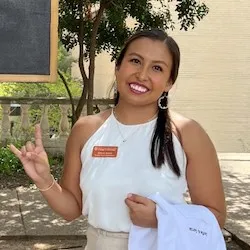 A woman with a white coat draped over him arm and giving the Hook 'em Horns hand gesture.