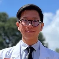 James Sagun wearing glasses and white coat and smiling.