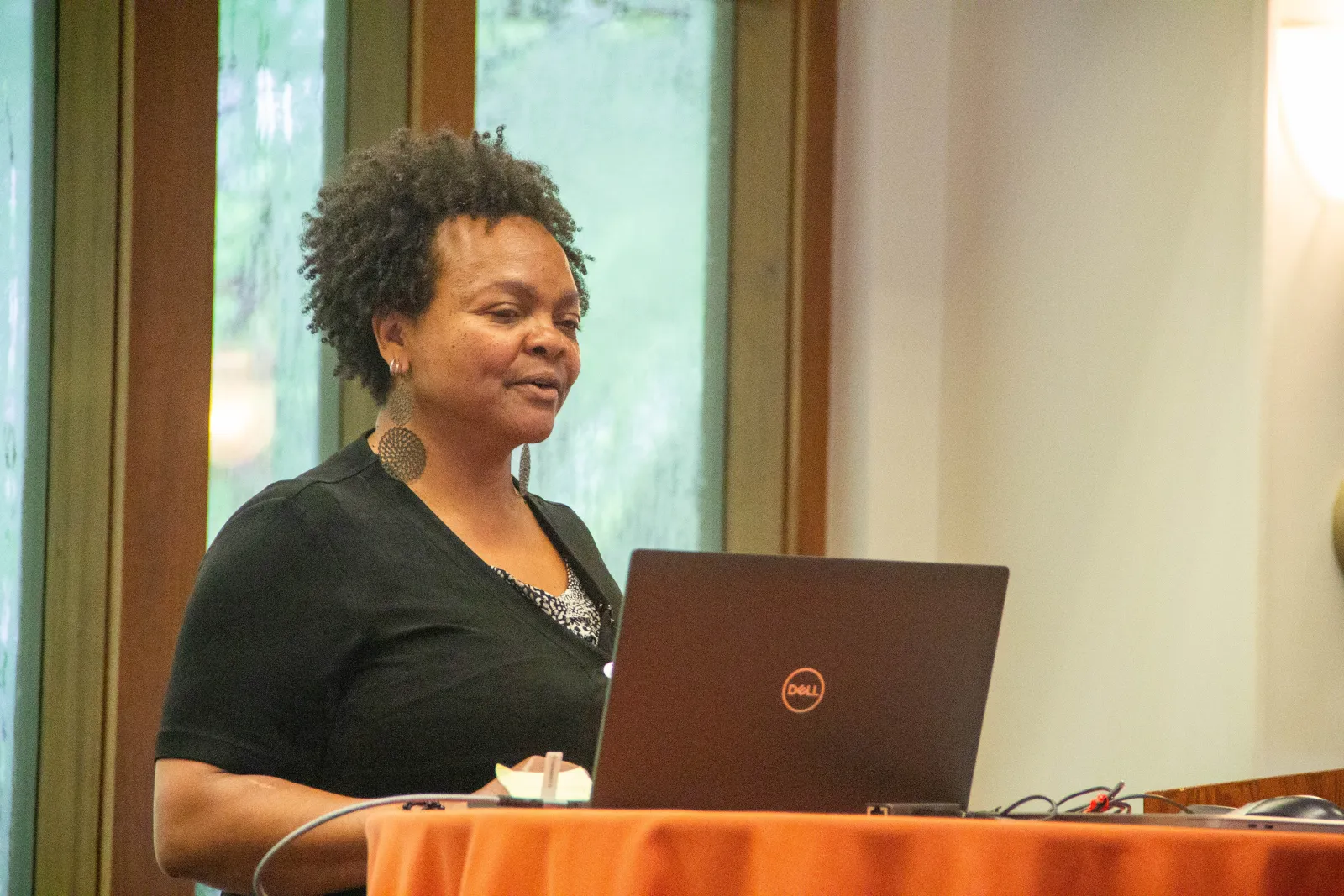 A woman wearing earrings giving a lecture in front of a laptop computer.