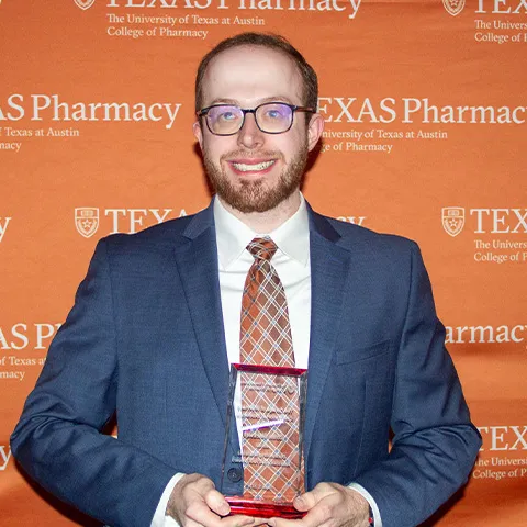A man in a suit and tie and glasses holding an award and smiling.