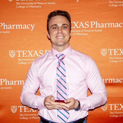 A man wearing a dress shirt and striped tie and smiling while holding an award.