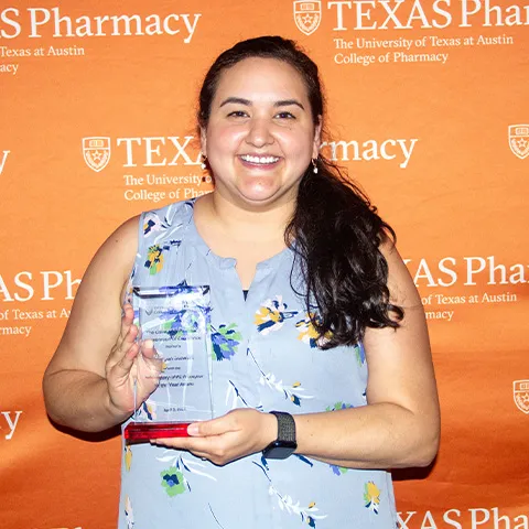 A woman wearing a sleeveless shirt and holding an award while smiling.