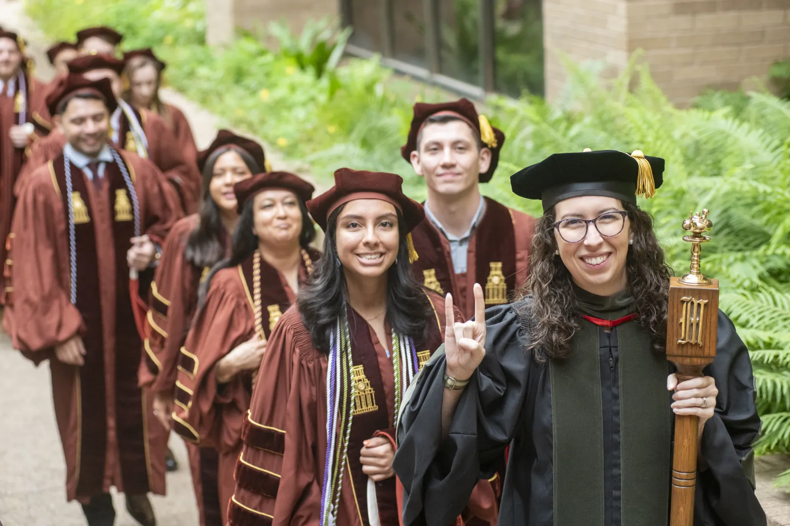 A line of people in their regalia giving the Hook 'em Horns.
