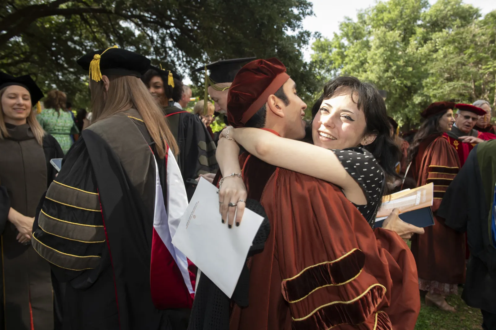 A woman hugging a man wearing regalia.