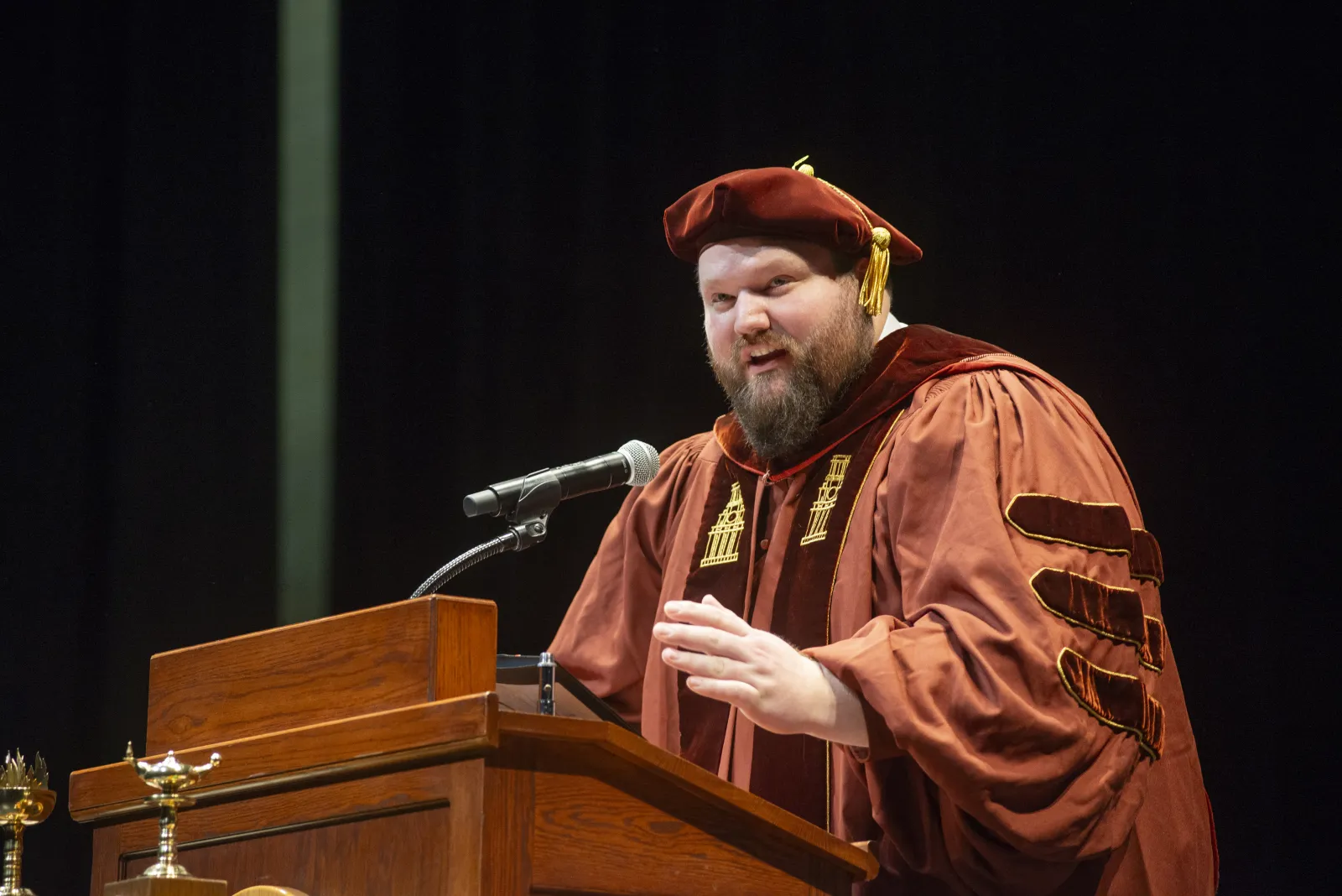 A man wearing regalia and giving a speech at a podium.