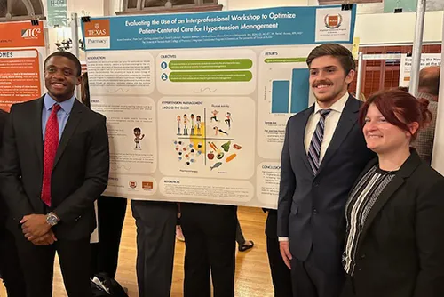 Three Pharm.D. students wearing suits and smiling next to their research poster