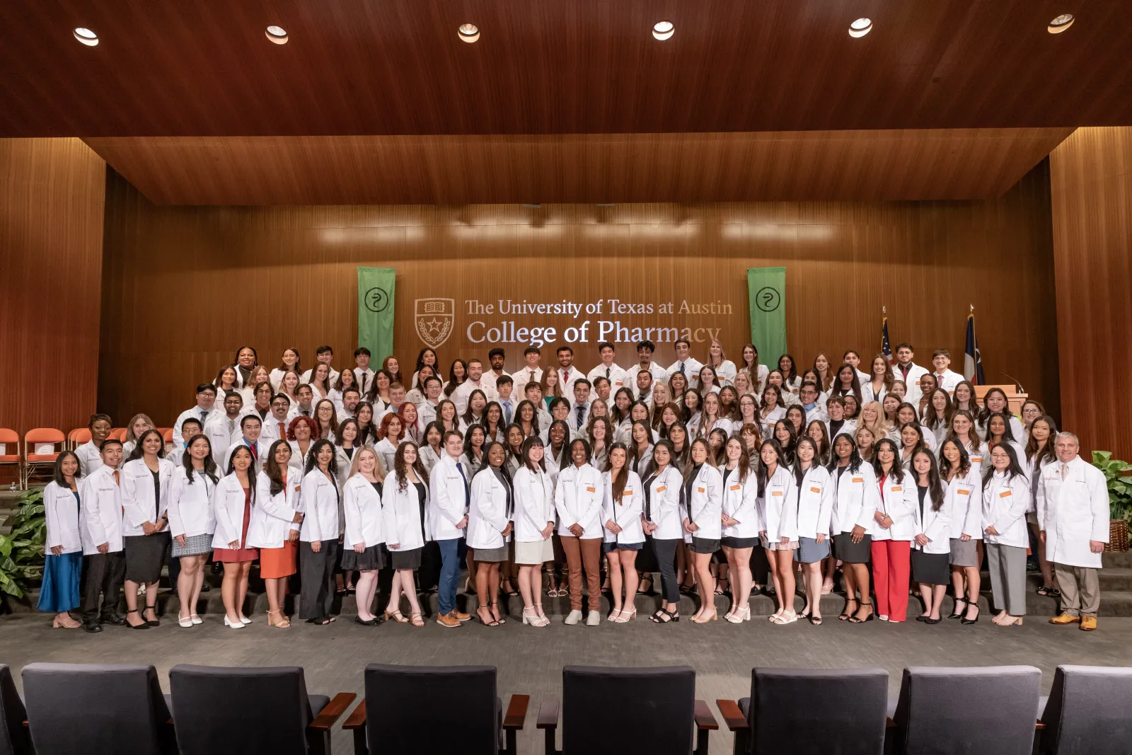 Class of 2028 group photo in white coats on the stage.