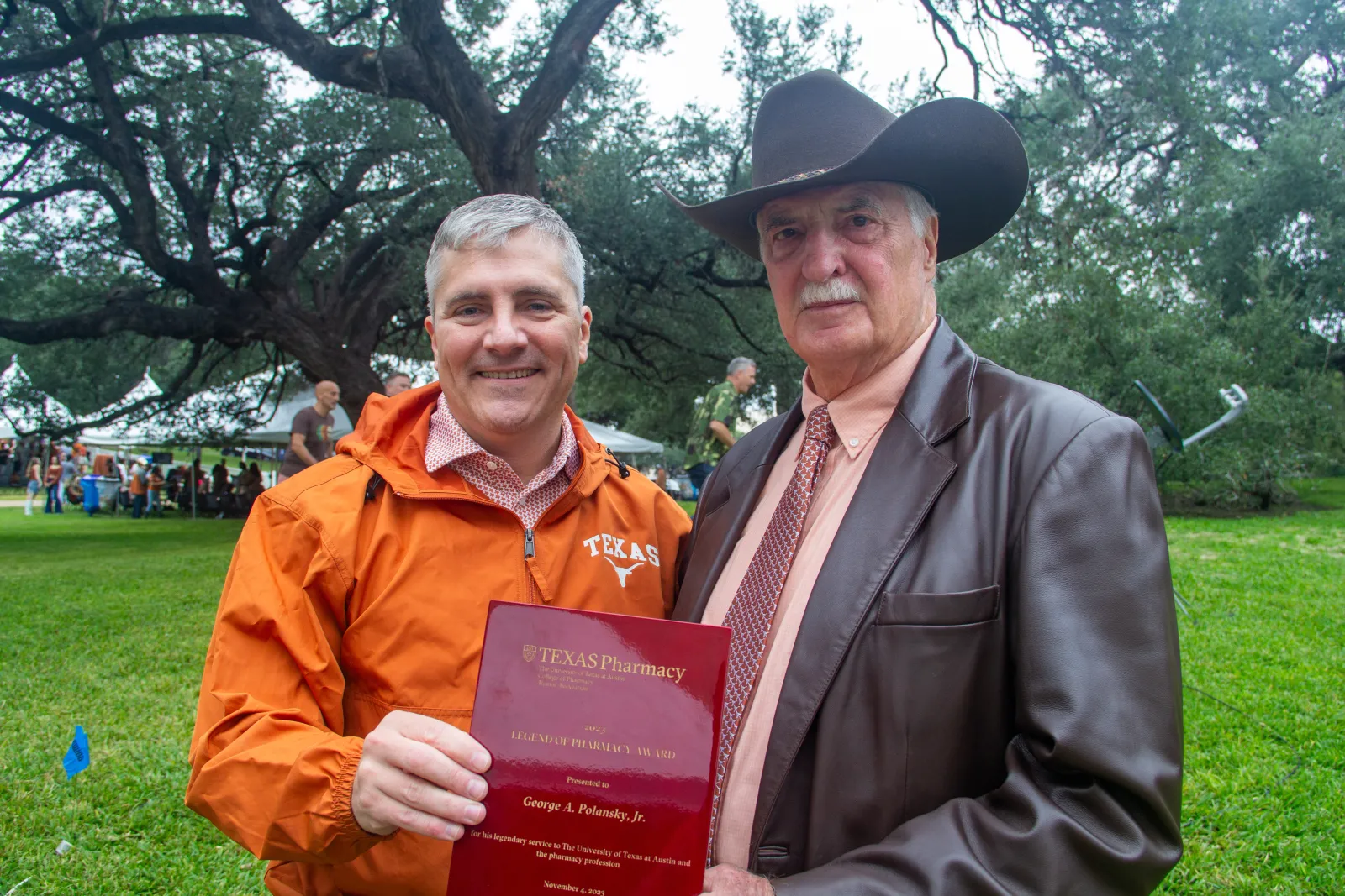 Dean Sam Poloyac and George Polanksy posing with George's award at the 2023 Texas Pharmacy Tailgate.
