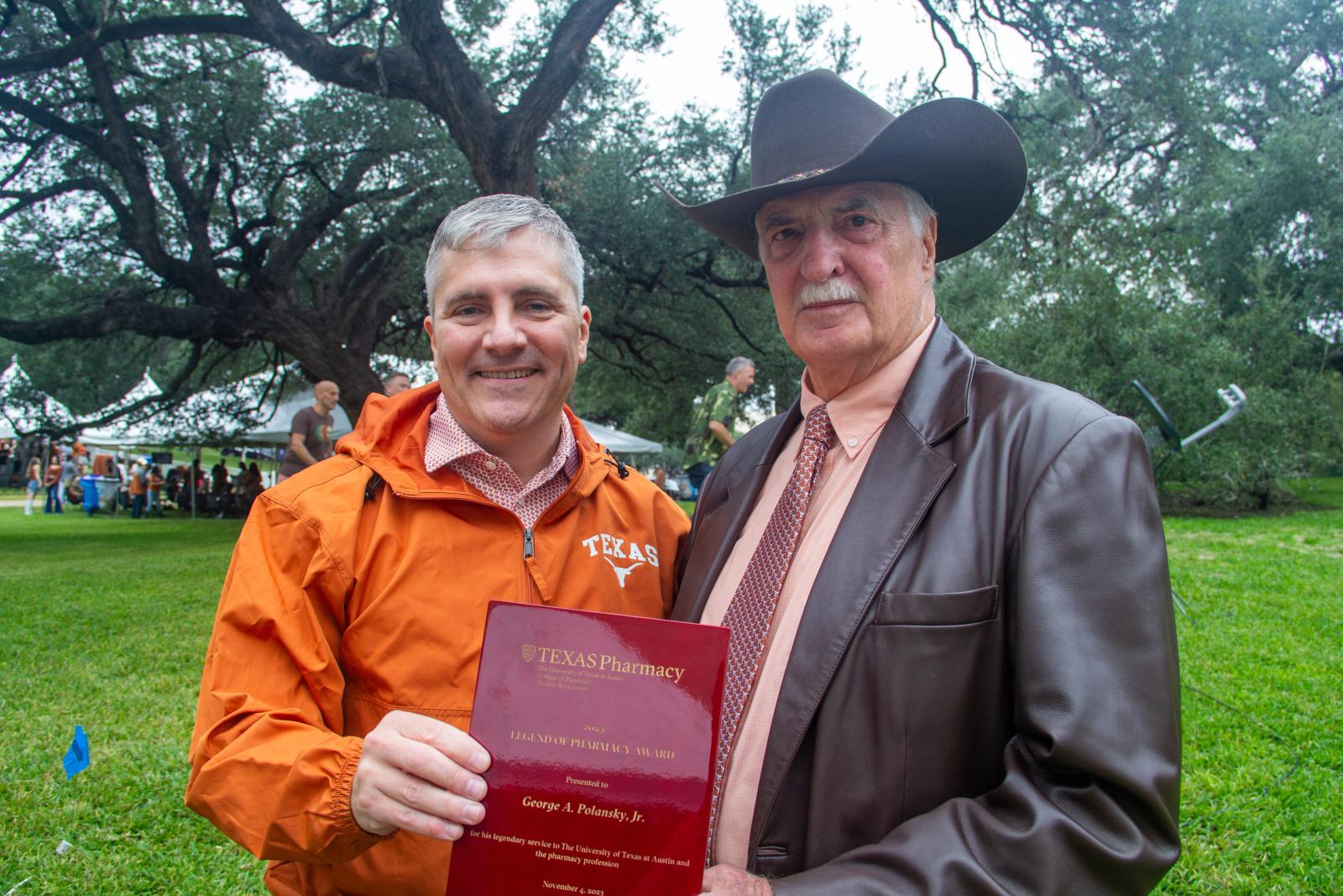 Dean Sam Poloyac and George Polanksy posing with George's award at the 2023 Texas Pharmacy Tailgate.