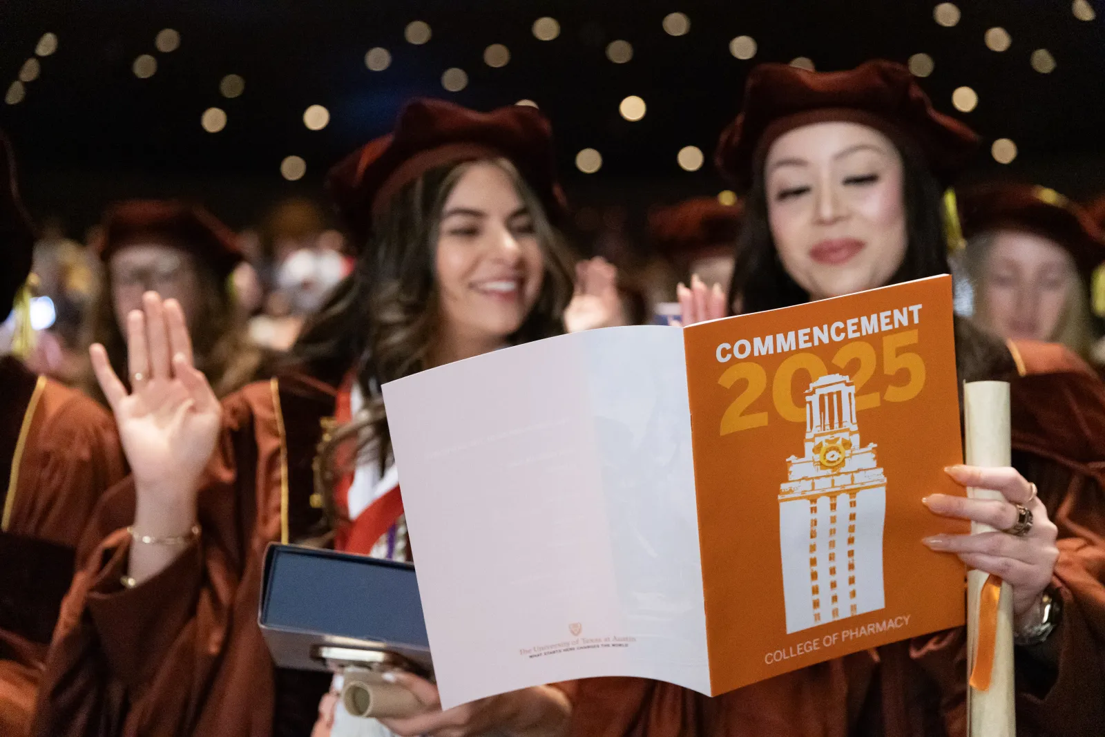 Students in regalia holding up the commencement program and reciting the Oath of a Pharmacist.
