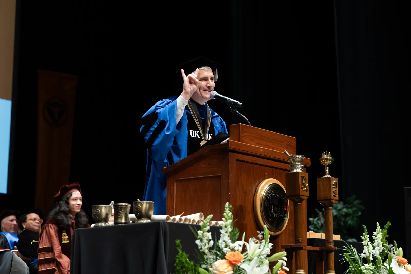 A man at a podium giving the Hook 'em hand gesture.